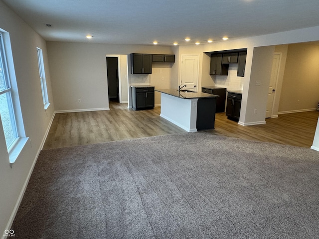 kitchen with decorative backsplash, light wood-type flooring, and an island with sink