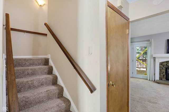 stairs featuring a stone fireplace and carpet