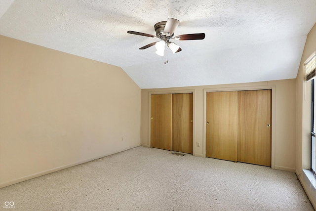 unfurnished bedroom featuring light carpet, two closets, ceiling fan, a textured ceiling, and vaulted ceiling