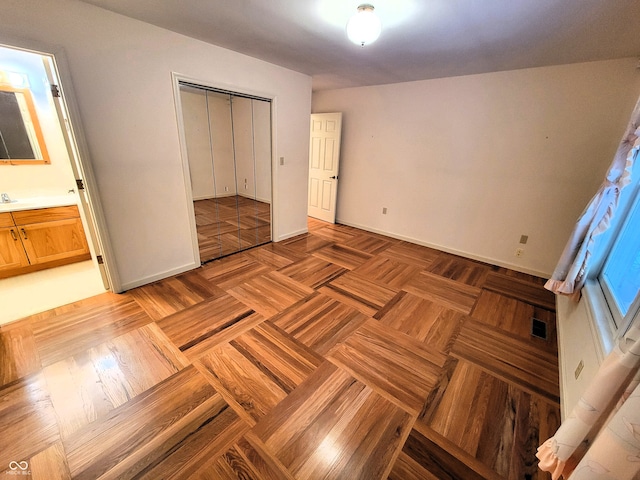 unfurnished bedroom with a closet, ensuite bath, sink, and light parquet flooring