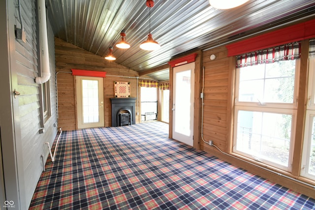 unfurnished living room featuring a healthy amount of sunlight, wooden walls, and vaulted ceiling