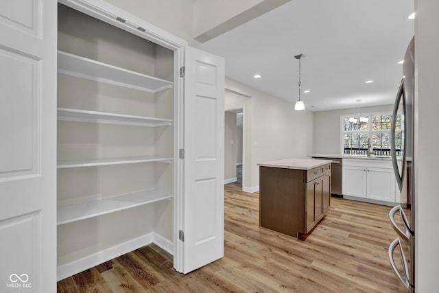 kitchen featuring appliances with stainless steel finishes, a center island, pendant lighting, a notable chandelier, and light hardwood / wood-style flooring