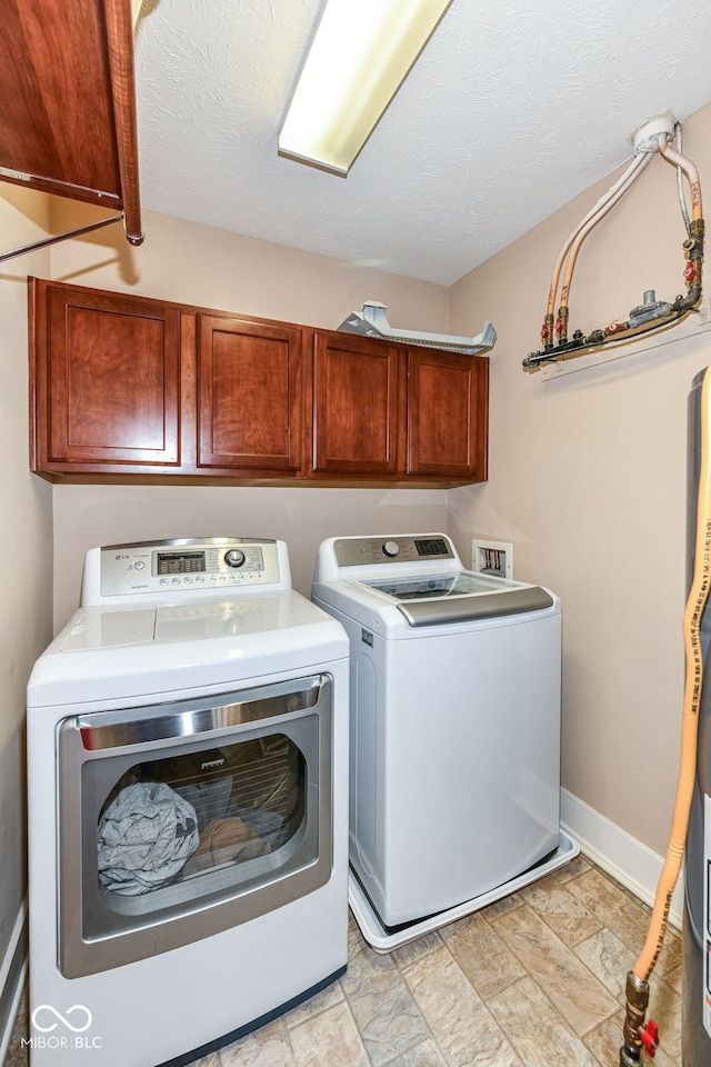 clothes washing area featuring washer and dryer, a textured ceiling, and cabinets