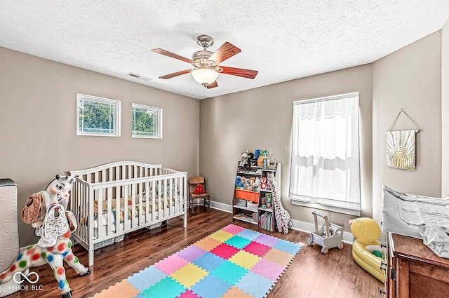 bedroom featuring a textured ceiling, a crib, dark wood-type flooring, and ceiling fan