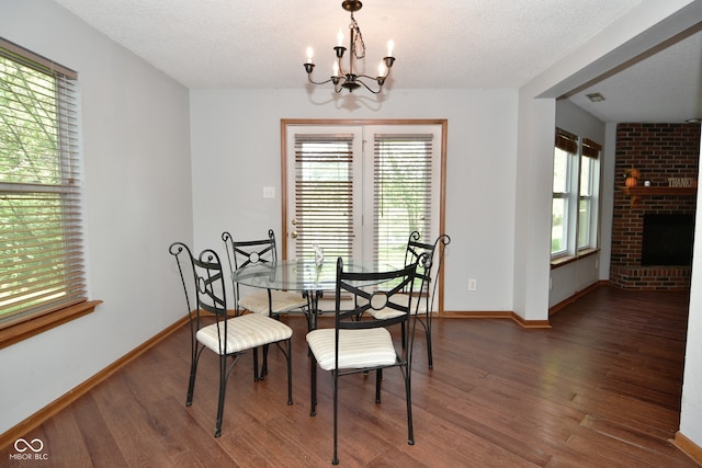 dining area with a fireplace, a textured ceiling, dark hardwood / wood-style flooring, and an inviting chandelier