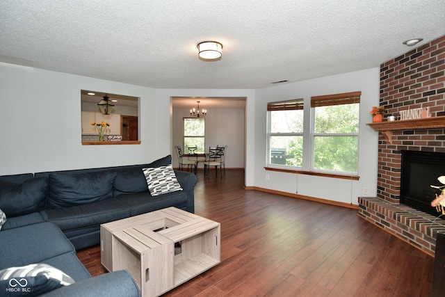 living room with a textured ceiling, dark hardwood / wood-style flooring, a brick fireplace, and an inviting chandelier