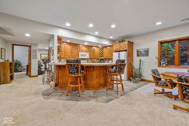 kitchen with kitchen peninsula, light colored carpet, and white appliances