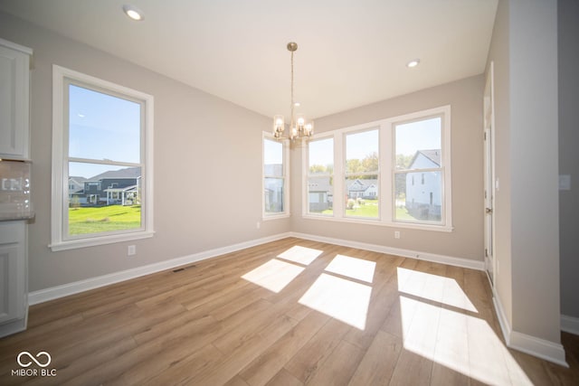 unfurnished dining area with a wealth of natural light, light hardwood / wood-style flooring, and an inviting chandelier