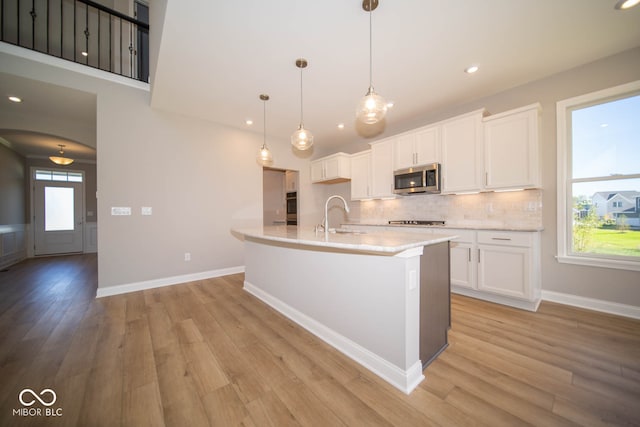 kitchen featuring sink, hanging light fixtures, stainless steel appliances, light hardwood / wood-style flooring, and white cabinets