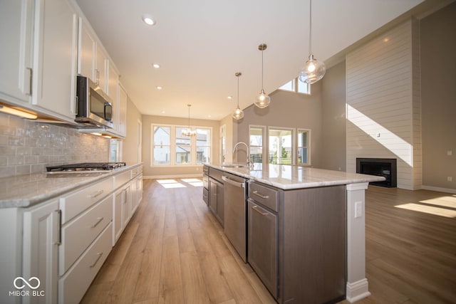 kitchen with white cabinetry, stainless steel appliances, hanging light fixtures, a kitchen island with sink, and a fireplace