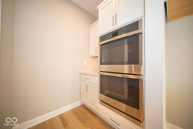 kitchen featuring white cabinets, light hardwood / wood-style floors, and stainless steel double oven