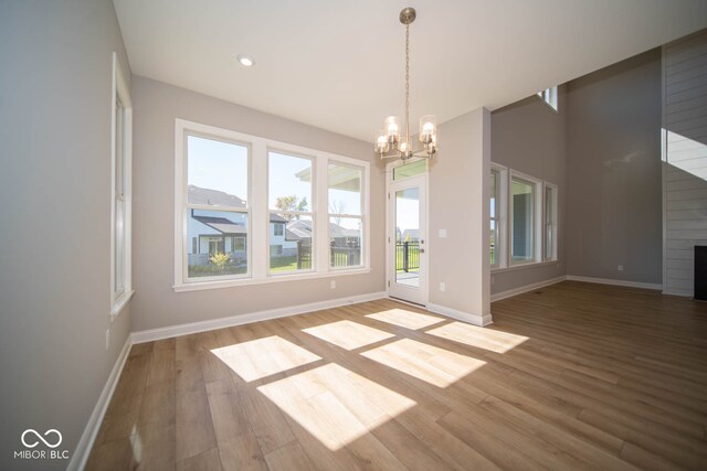 unfurnished dining area featuring wood-type flooring, a large fireplace, and a notable chandelier