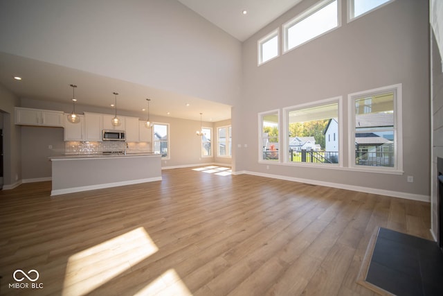 unfurnished living room with a chandelier, light hardwood / wood-style flooring, and high vaulted ceiling