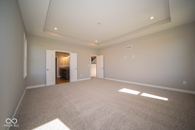 unfurnished bedroom featuring ensuite bathroom, carpet floors, and a tray ceiling