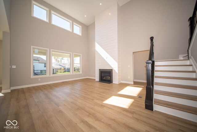 unfurnished living room featuring light hardwood / wood-style floors, a towering ceiling, and a fireplace