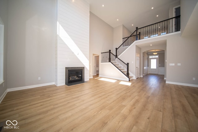 unfurnished living room with light hardwood / wood-style floors, a towering ceiling, and a tiled fireplace