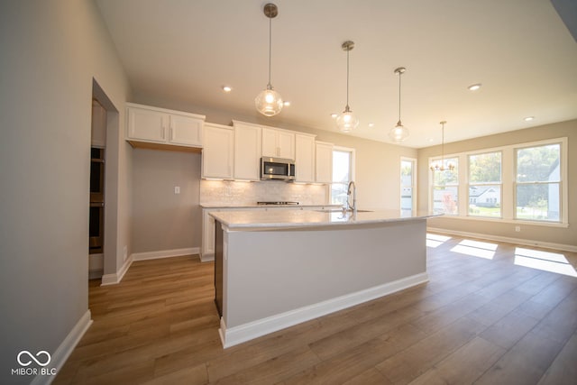 kitchen with pendant lighting, white cabinetry, stainless steel appliances, and a kitchen island with sink