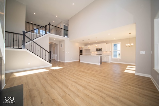 unfurnished living room with a high ceiling, light wood-type flooring, and an inviting chandelier