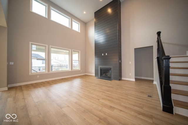 unfurnished living room featuring a large fireplace, a towering ceiling, and light hardwood / wood-style flooring