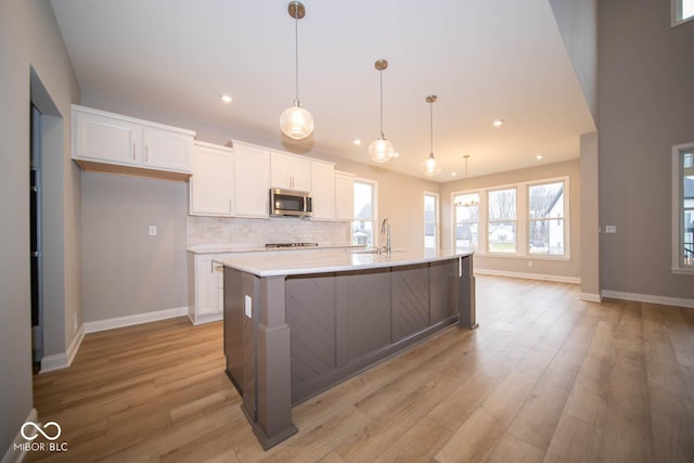 kitchen with pendant lighting, light wood-type flooring, white cabinetry, and an island with sink