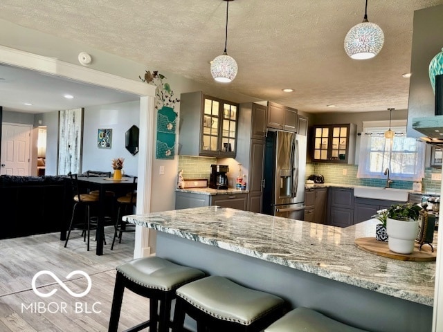 kitchen featuring kitchen peninsula, stainless steel fridge, hanging light fixtures, and light wood-type flooring