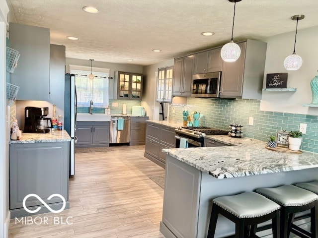 kitchen featuring light hardwood / wood-style flooring, kitchen peninsula, gray cabinetry, pendant lighting, and appliances with stainless steel finishes