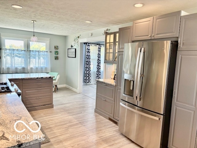 kitchen featuring stainless steel fridge, light stone countertops, decorative light fixtures, light wood-type flooring, and gray cabinets