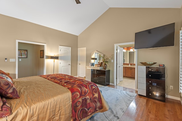 bedroom featuring light wood-type flooring, baseboards, ceiling fan, ensuite bath, and high vaulted ceiling