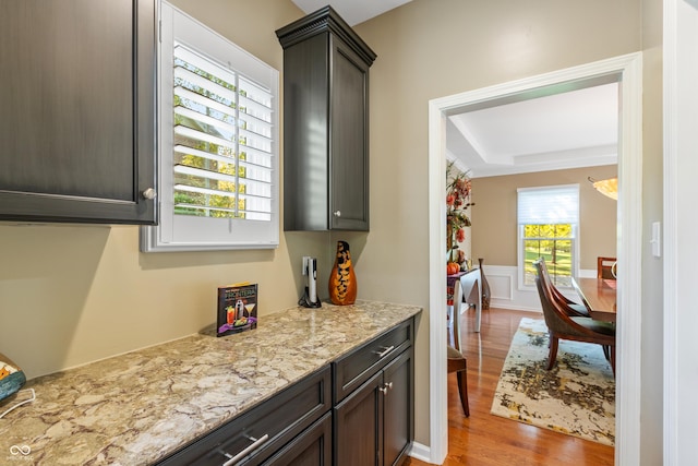 kitchen featuring wainscoting, wood finished floors, dark brown cabinets, and light stone counters