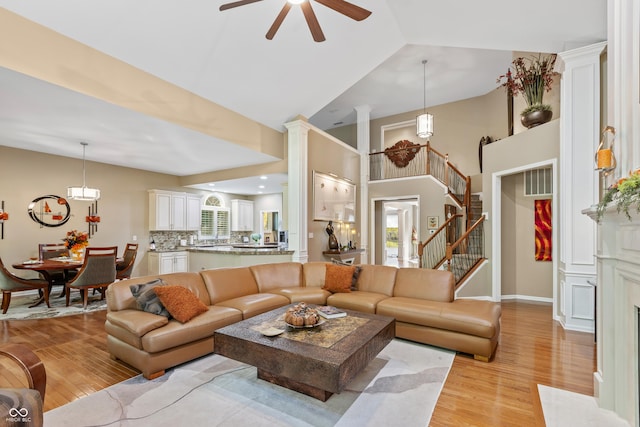 living area featuring high vaulted ceiling, stairs, ceiling fan, light wood finished floors, and baseboards