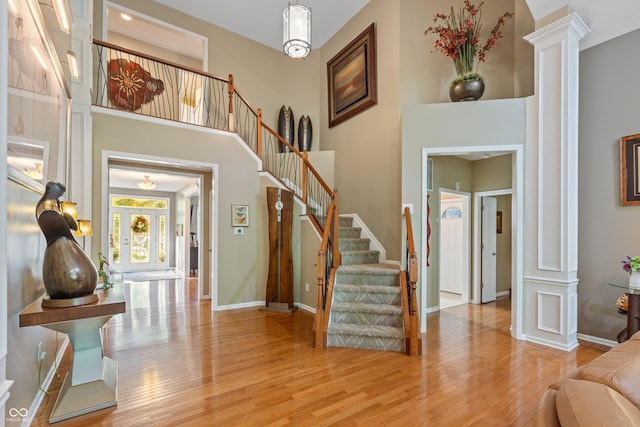 entryway featuring light wood finished floors, stairway, a towering ceiling, and ornate columns
