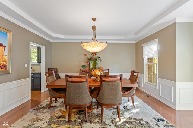 dining area with a tray ceiling, light wood-type flooring, visible vents, and wainscoting
