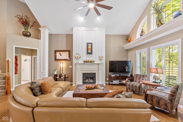 living area with a ceiling fan, wood finished floors, a glass covered fireplace, a high ceiling, and ornate columns