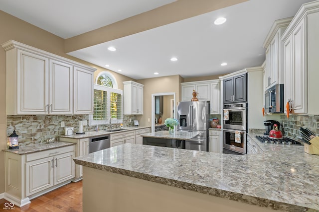 kitchen featuring light wood finished floors, light stone counters, stainless steel appliances, a sink, and tasteful backsplash
