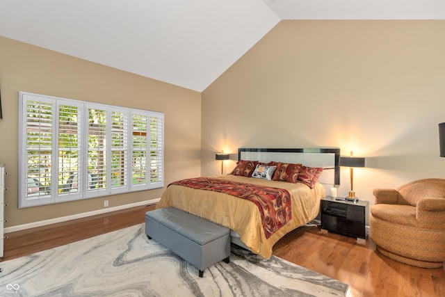 bedroom with high vaulted ceiling, wood finished floors, and baseboards
