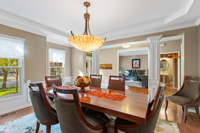 dining space with light hardwood / wood-style floors, a raised ceiling, decorative columns, and ornamental molding