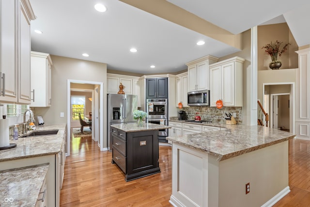 kitchen featuring appliances with stainless steel finishes, sink, light wood-type flooring, a kitchen island, and light stone counters