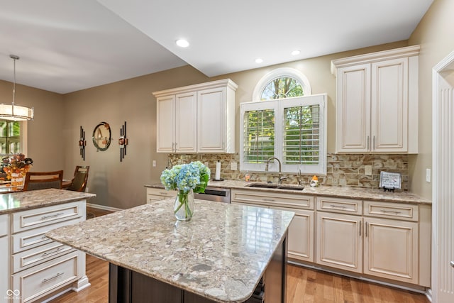 kitchen with decorative backsplash, light stone countertops, a sink, and light wood finished floors