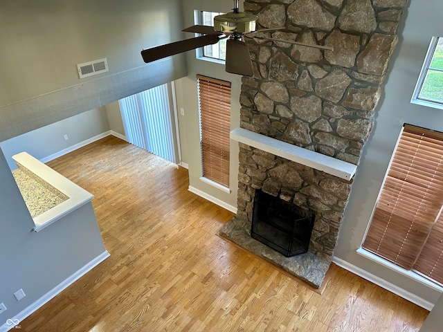 living room with hardwood / wood-style flooring, ceiling fan, a stone fireplace, and a towering ceiling