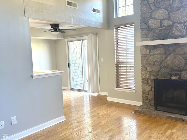 unfurnished living room featuring a towering ceiling, light wood-type flooring, a stone fireplace, and ceiling fan