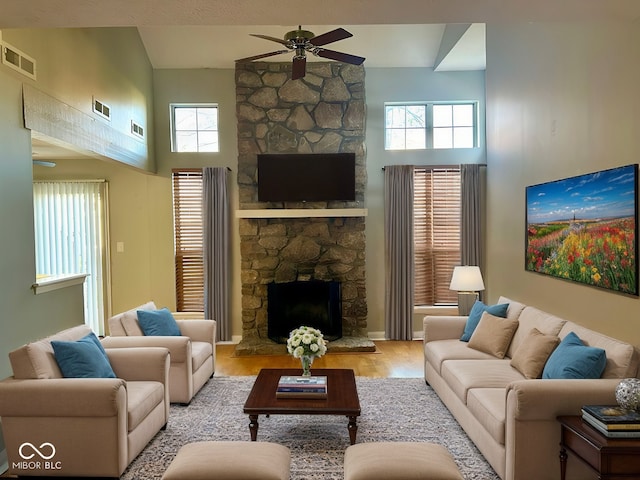 living room featuring a stone fireplace, ceiling fan, light hardwood / wood-style flooring, and a towering ceiling