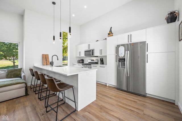 kitchen featuring kitchen peninsula, white cabinets, stainless steel appliances, light hardwood / wood-style floors, and decorative light fixtures