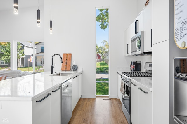 kitchen with white cabinets, hanging light fixtures, light hardwood / wood-style flooring, sink, and stainless steel appliances