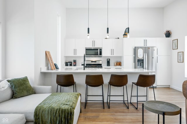 kitchen with white cabinetry, stainless steel appliances, a breakfast bar, and hanging light fixtures