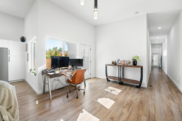 office area with light hardwood / wood-style floors and a towering ceiling