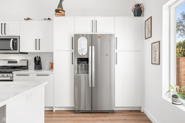 kitchen featuring white cabinetry, light stone counters, stainless steel appliances, and light hardwood / wood-style floors