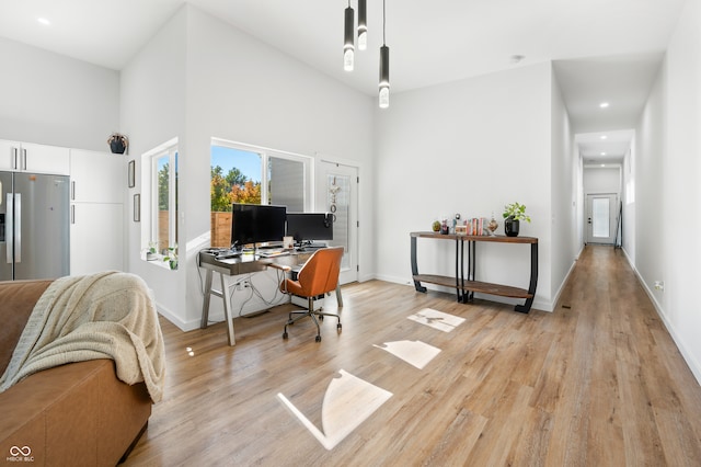 office featuring a towering ceiling and light hardwood / wood-style floors