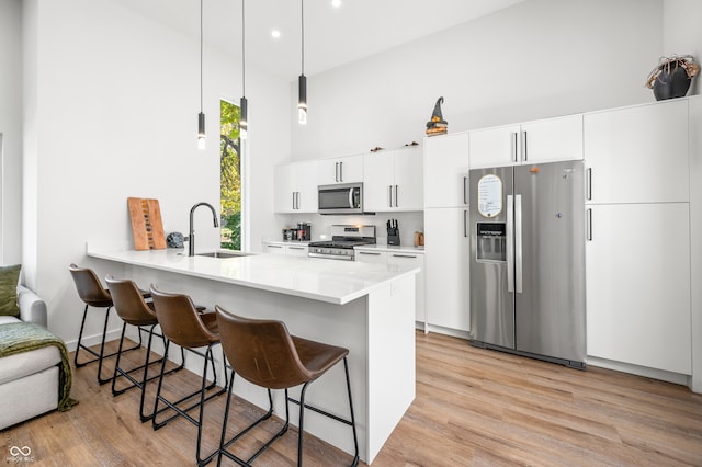 kitchen featuring appliances with stainless steel finishes, sink, kitchen peninsula, pendant lighting, and white cabinets