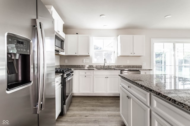 kitchen with white cabinetry, appliances with stainless steel finishes, stone countertops, and sink