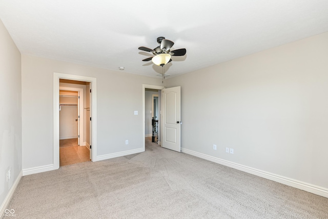 unfurnished bedroom featuring a spacious closet, a closet, ceiling fan, and light colored carpet